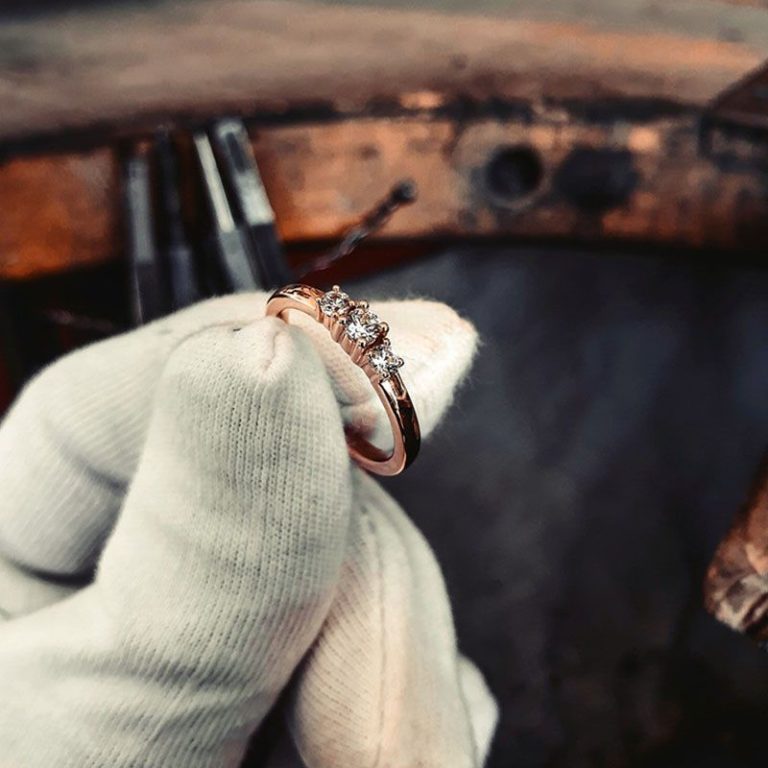 Eine Hand mit weißen Baumwollhandschuhe hält einen goldenen Diamantring